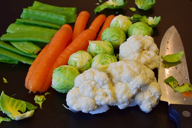 Cauliflower heads, Brussels sprouts, carrots and sugar snap peas on a table prepared for juicing.